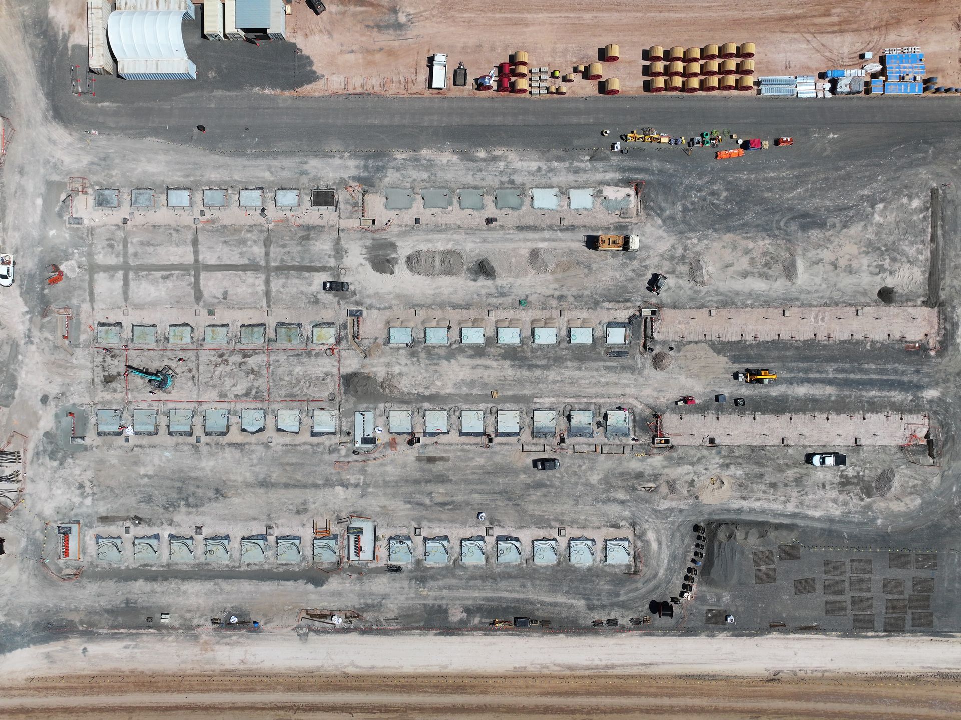 Aerial view of a construction site with rows of concrete foundations, machinery, and stacked materials.