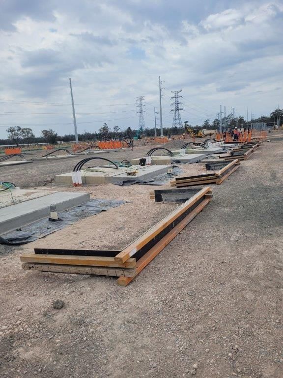 Construction site with concrete forms, rebar, and equipment laid out on a dirt road under an overcast sky