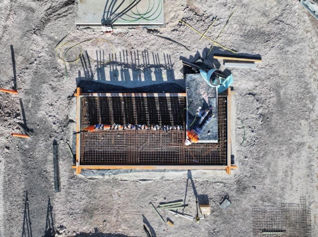 Aerial view of a construction site with rebar framework and workers’ equipment on gravel.