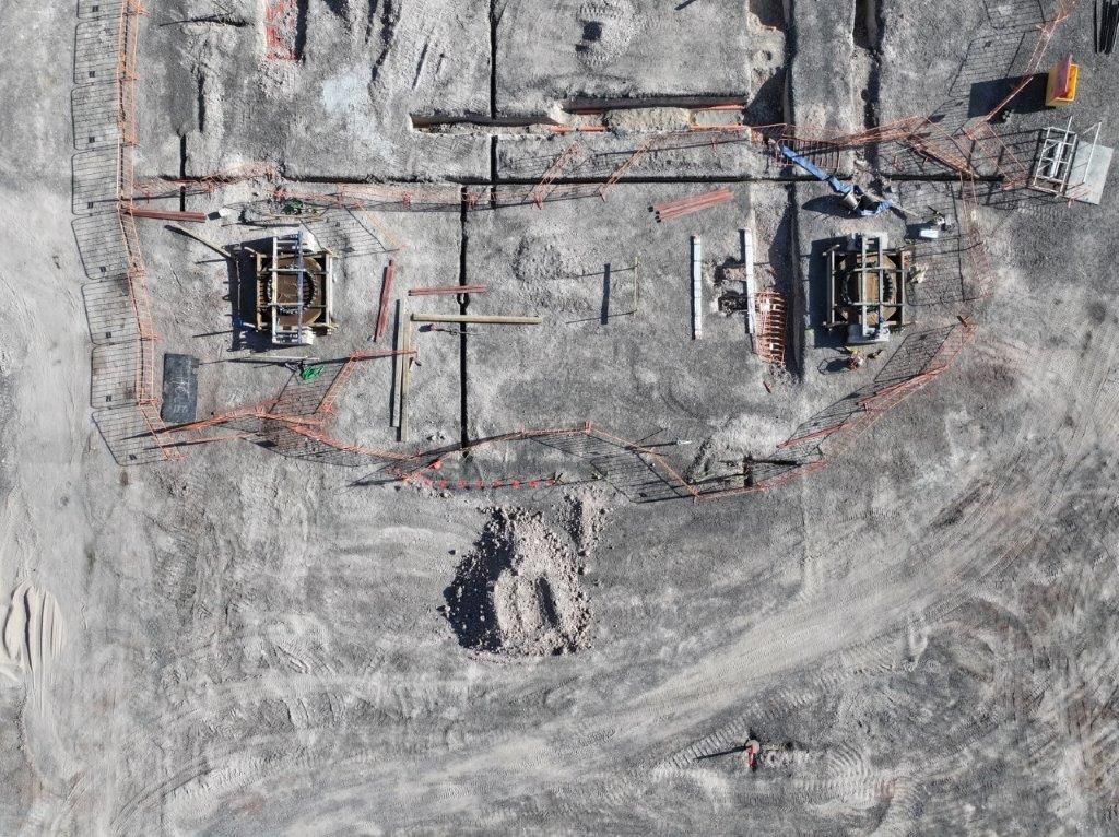 Aerial view of a dusty construction site with two excavators and marked excavation areas.