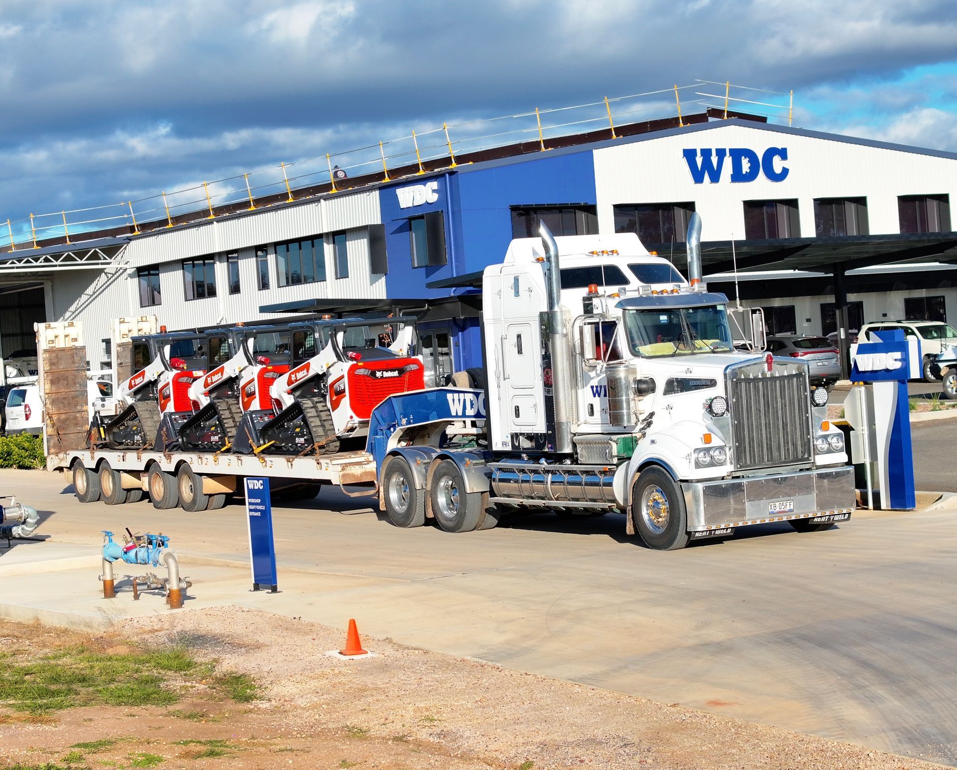 White WDC semi truck with red equipment parked outside a warehouse under a blue sky