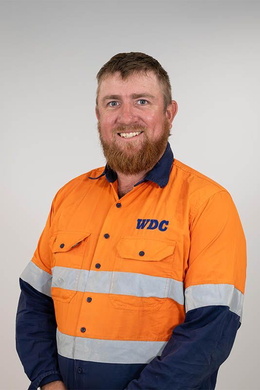 Worker in orange high-vis shirt and navy sleeves, smiling against a plain background.