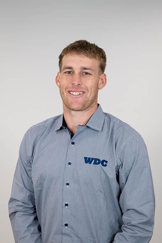 Smiling person in a blue button-down shirt with a WDC logo against a gray background