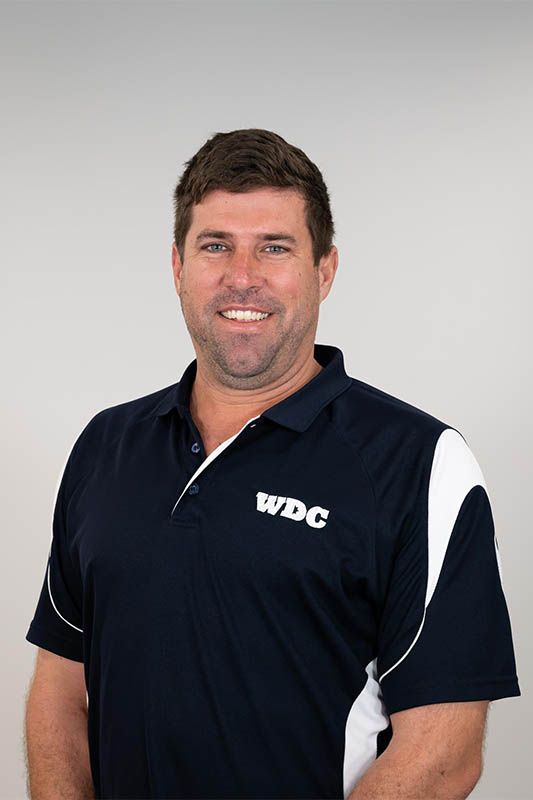 Man in a navy WDC polo shirt smiling against a light gray background