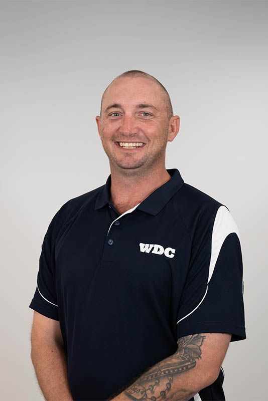 Smiling man in a navy polo shirt with white trim against a plain gray background