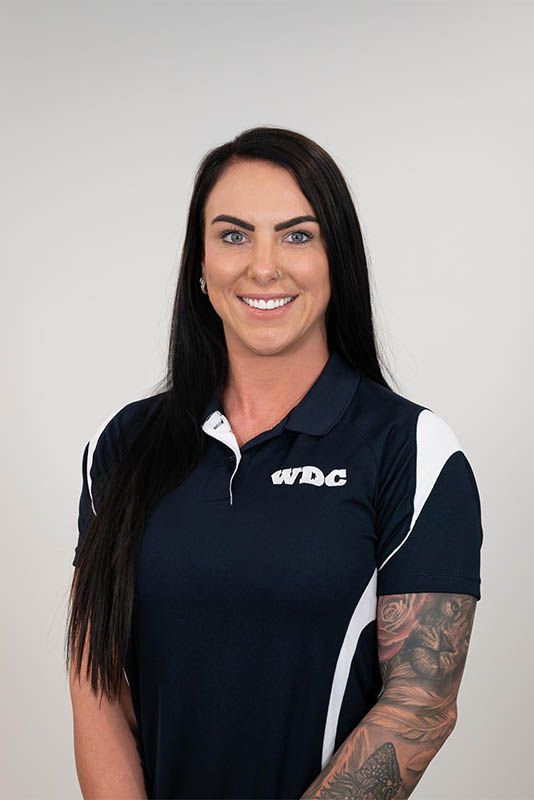 Woman in a black and white polo shirt with a tattooed arm, smiling against a plain gray background.