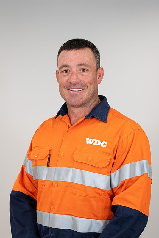 Man in orange and navy work uniform with reflective stripes, smiling against a plain background