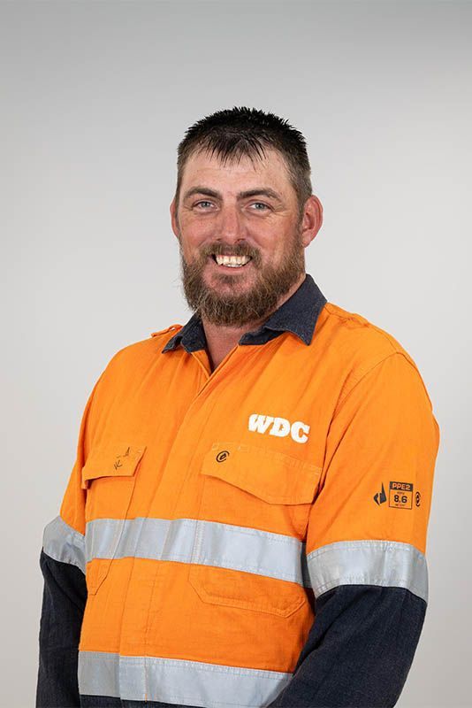 Man in orange high-visibility work shirt smiling against a plain gray background