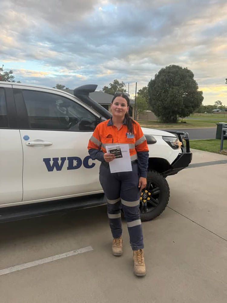 Person in orange safety gear standing beside a WDC utility truck outdoors.