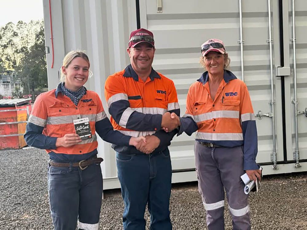 Three workers in orange safety uniforms standing beside a shipping container, smiling at the camera