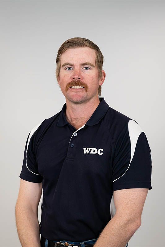 Man in a navy WDC polo shirt standing against a light gray background