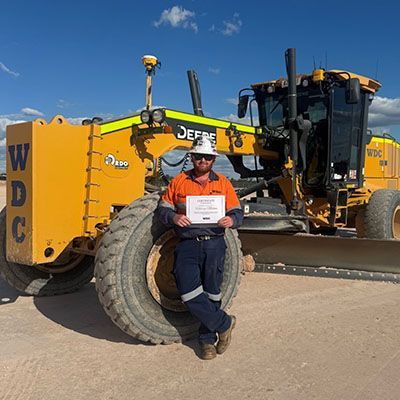 Person sitting on a yellow JCB construction machine, holding a sign, in bright sunlight.