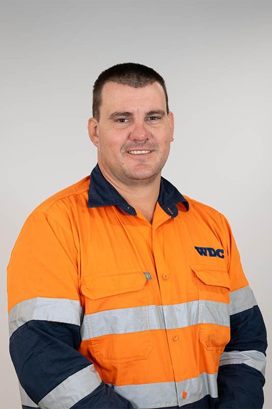 Man in orange high-visibility work shirt standing against a plain gray background