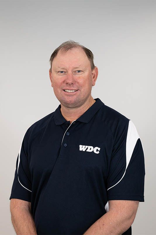 Man in a navy WDC polo shirt standing against a light gray background