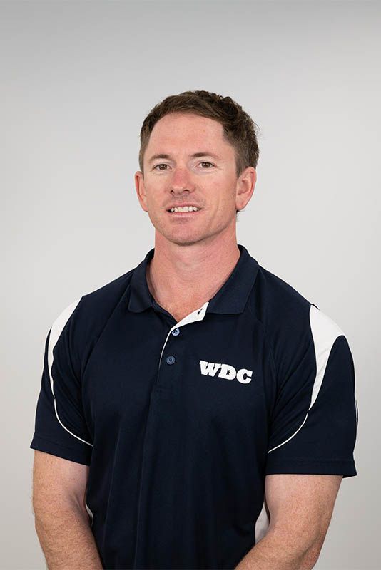 Man in navy polo shirt with white accents and WDC logo standing against a light gray background