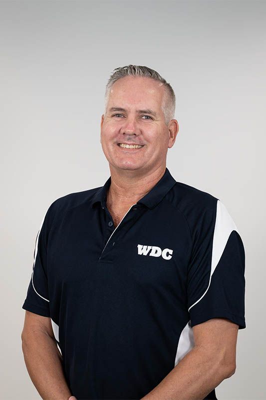 Smiling man in a navy WDC polo shirt standing against a light gray background
