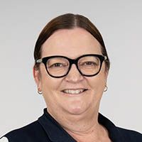 Smiling person with dark hair and black glasses against a light gray background