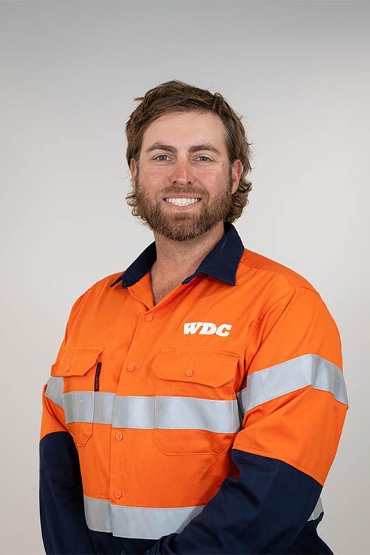 Smiling worker in orange high-vis jacket with reflective stripes and navy sleeves against a gray background