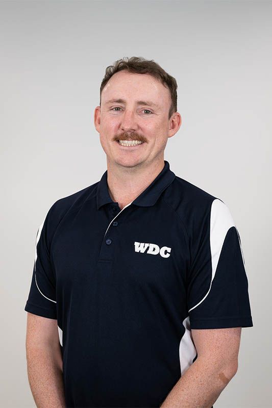 Man in navy polo shirt with white accents and WDC logo, standing against a light gray background