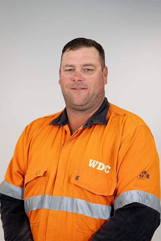 Worker in orange WDC safety jacket, standing against a plain gray background.