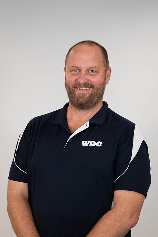 Smiling man in a navy polo shirt standing against a light gray background
