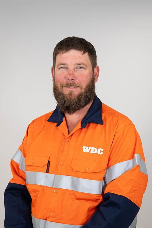 Man in an orange and navy high-visibility work shirt against a plain gray background.