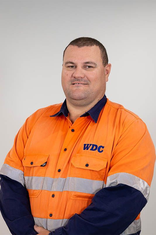 Worker in orange WDC uniform standing against a gray background.