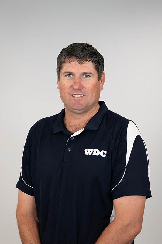 Man wearing a navy WDC polo shirt, standing against a light gray background.
