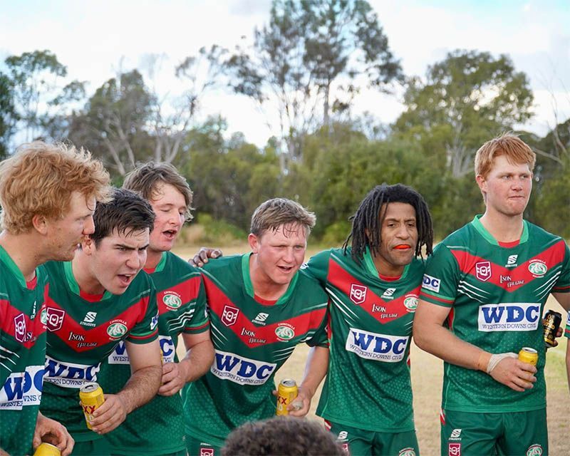 Green-uniformed rugby players huddle on a field, smiling and talking during a match break.