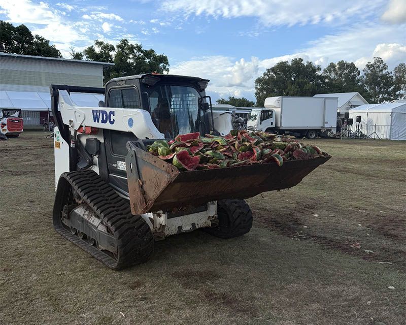 Tracked skid steer with raised bucket full of mulch at an outdoor worksite.