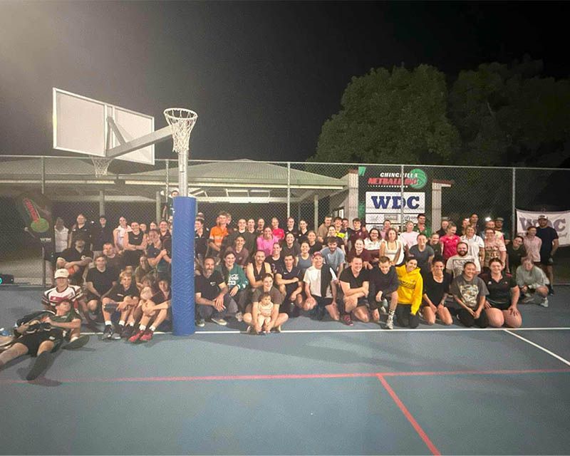 Large group posing on an outdoor basketball court at night, with a hoop and a WDC sign in the background