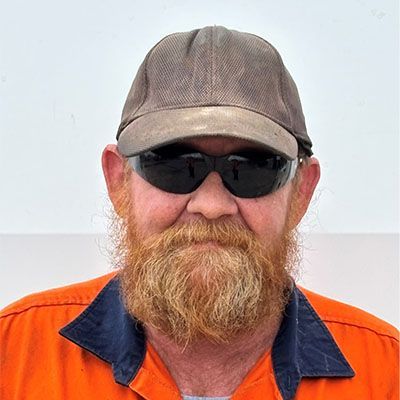 Man wearing a gray cap, black sunglasses, and orange jacket, with a red beard, against a light background