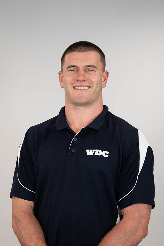 Man in a navy WDC polo shirt standing against a light gray background, smiling at the camera