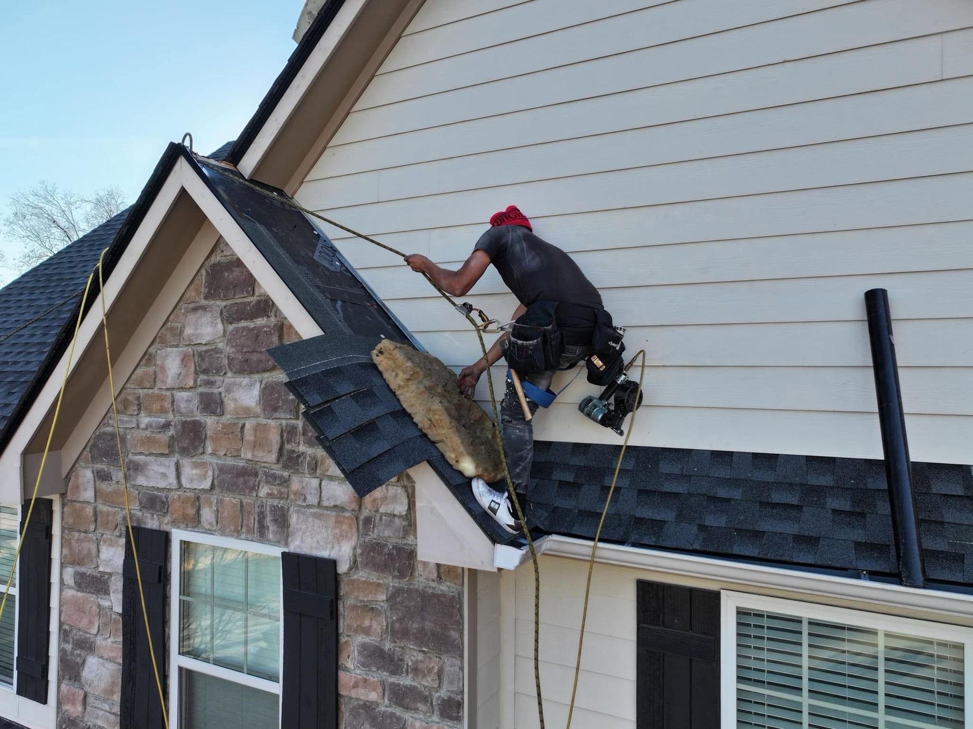 Worker repairing roof shingles on a house roof beside a stone chimney