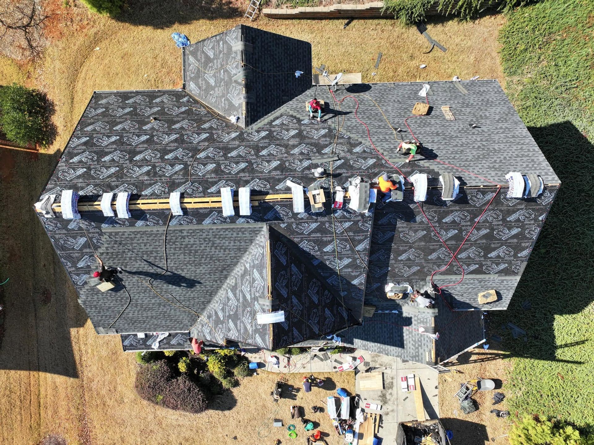 Aerial view of a dark-shingled house roof with several workers and construction materials on top.