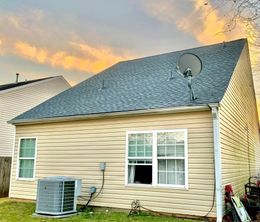 Suburban house with beige siding and a textured gray roof at sunset, with an outdoor AC unit and satellite dish