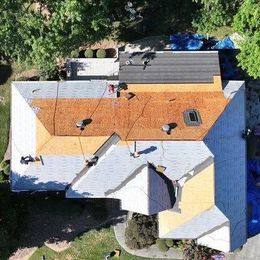 Aerial view of a house roof with orange, white, and gray sections, vents, and a central chimney.