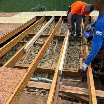 Workers repairing a wooden roof deck with exposed beams and boards on a rooftop.