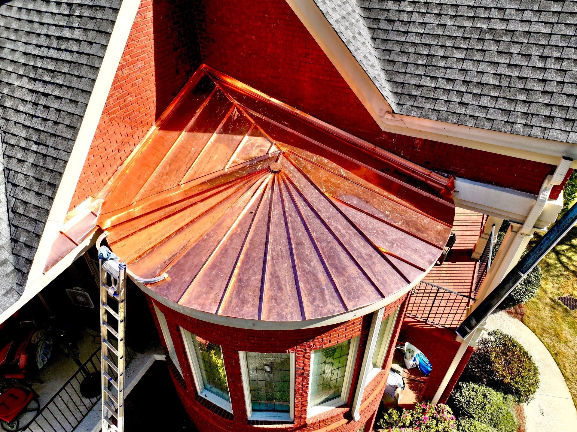 Aerial view of a red octagonal turret with a copper roof beside gray shingled rooftops.