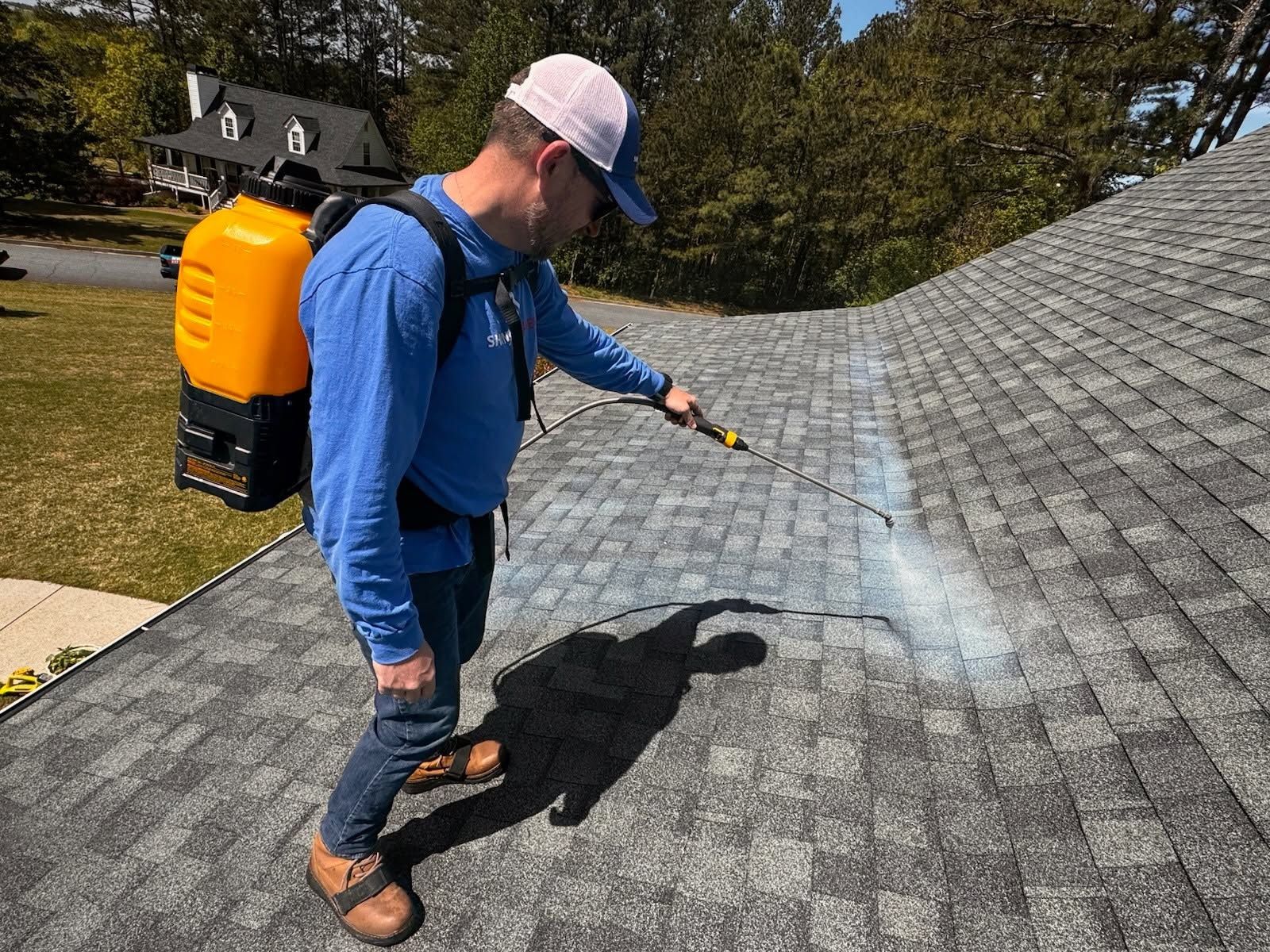 Person spraying treatment on a shingled roof with a backpack sprayer
