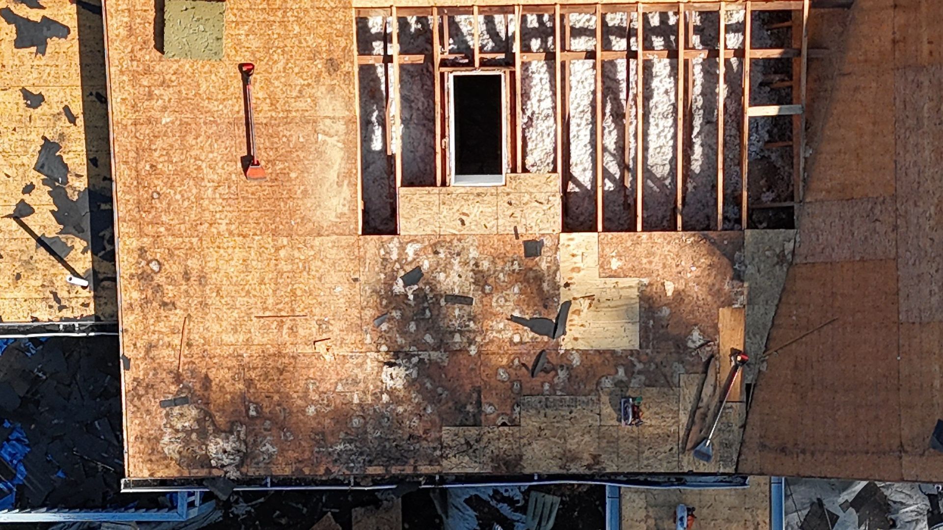 Damaged rooftop with debris, a small window, and exposed beams in warm sunlight