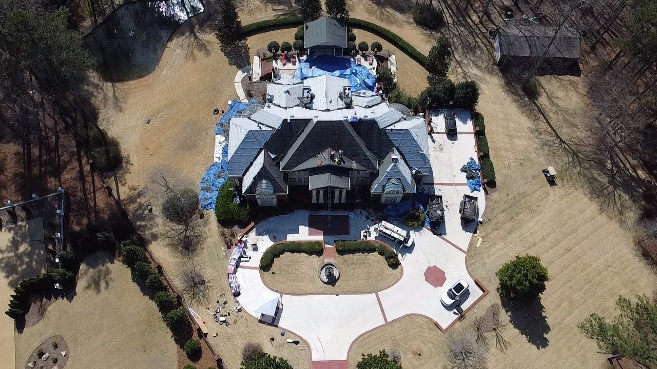 Aerial view of a circular outdoor pavilion with white patio, blue accents, and surrounding trees and lawn