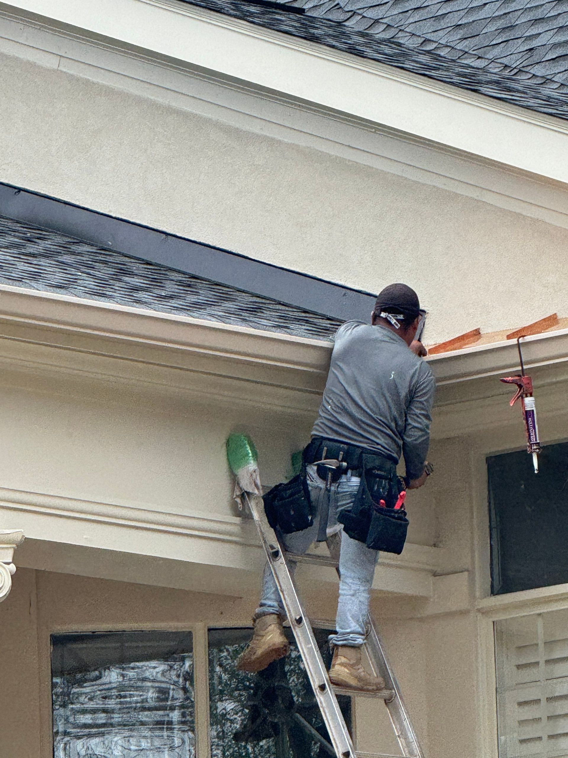 Worker on a ladder painting trim on a house exterior