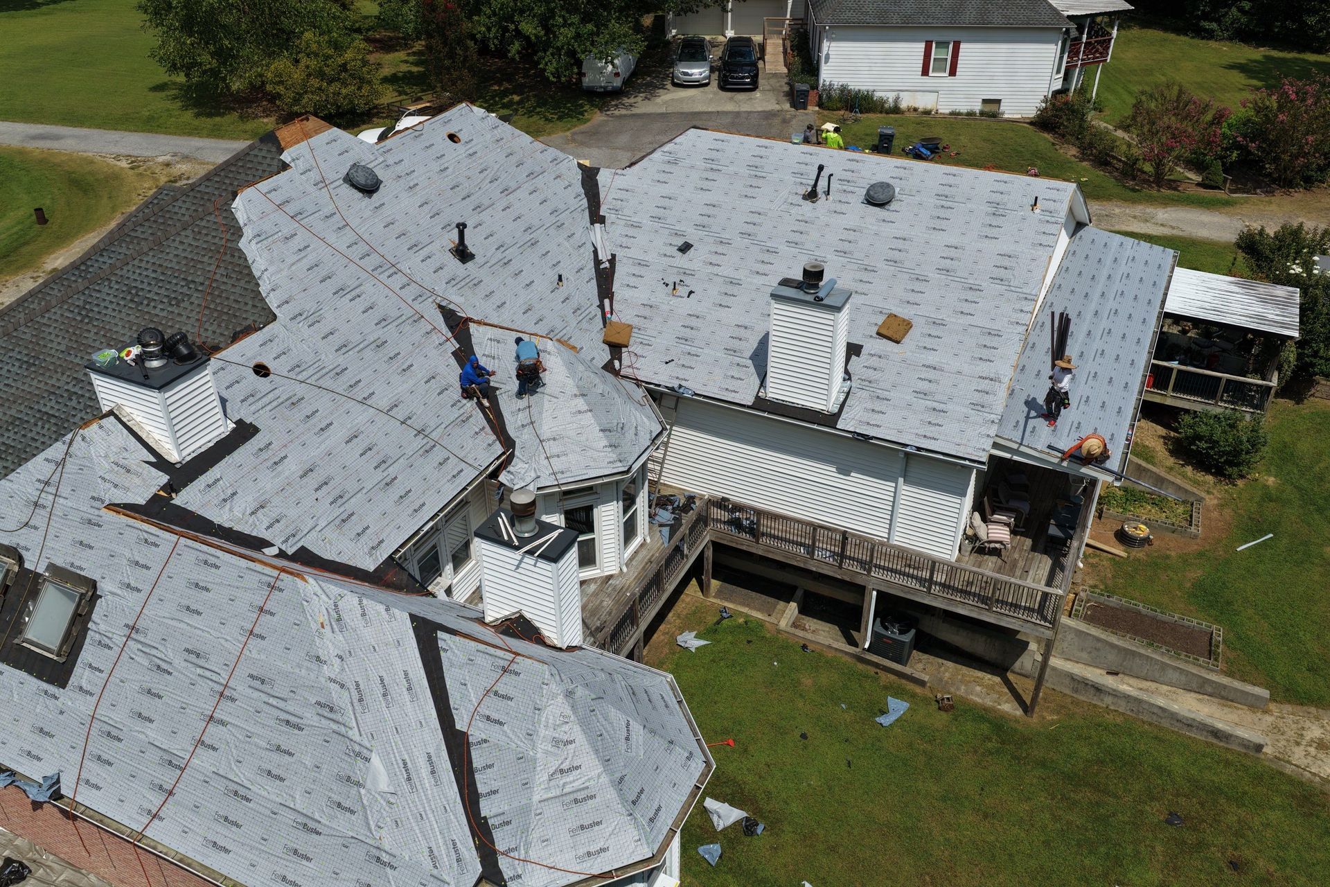 Aerial view of workers repairing a large gray-roofed house with scaffolding and tools.