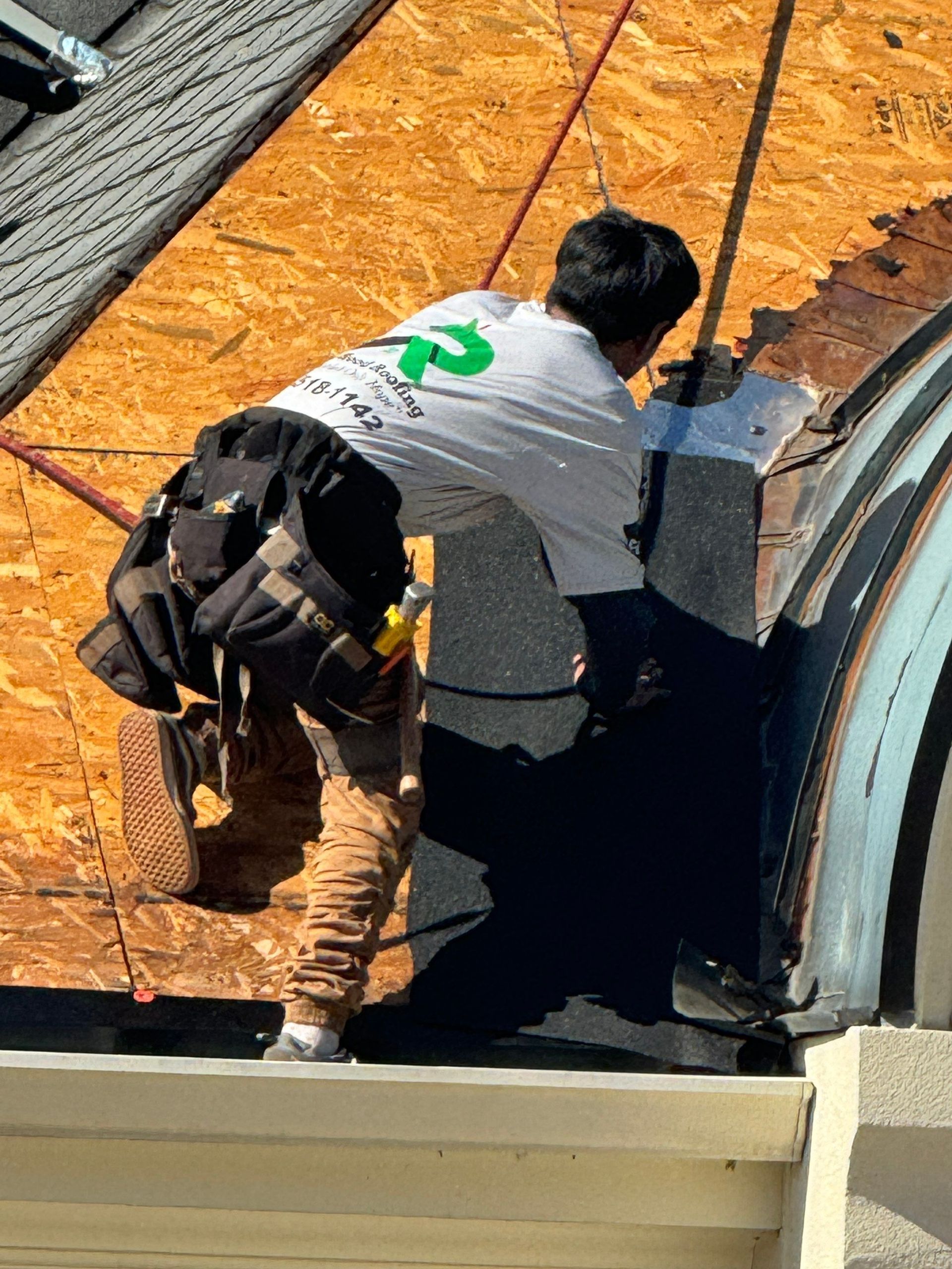 Worker kneeling on a roof, repairing a hole beside orange underlayment and gray shingles.