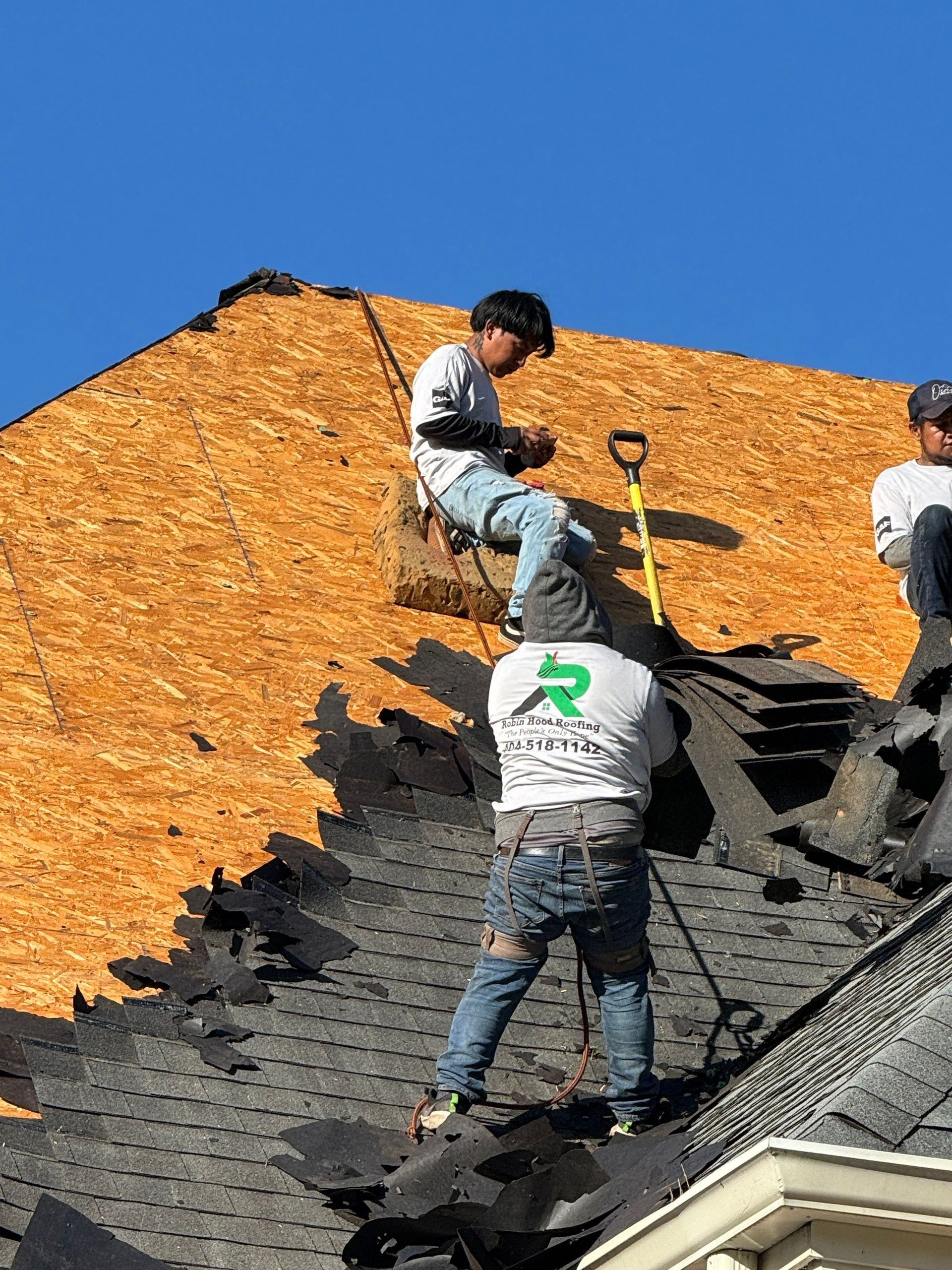 Workers roofing a house, laying black shingles beneath orange roof sheathing.