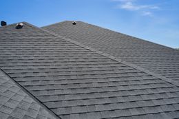 Gray shingled roof under a clear blue sky with a small dormer vent