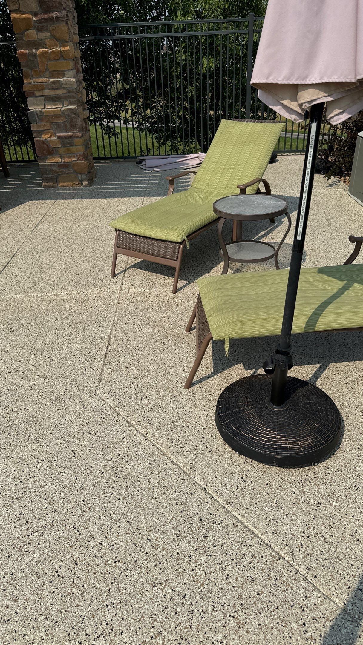 Patio with green lounge chairs, a small side table, and a closed umbrella on gravel.