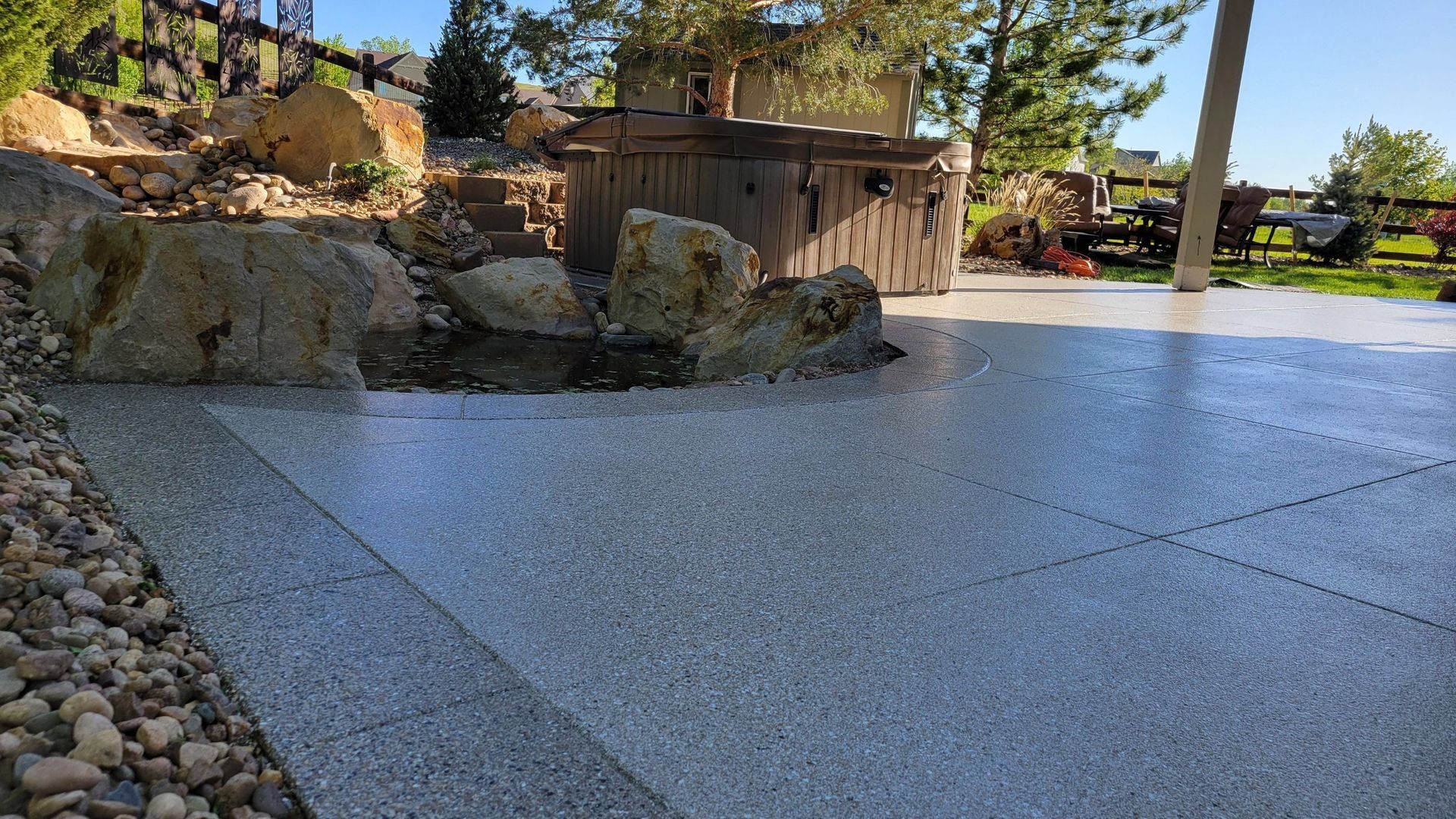 Stone patio beside rocks and a wooden planter, with trees and lawn in the background.
