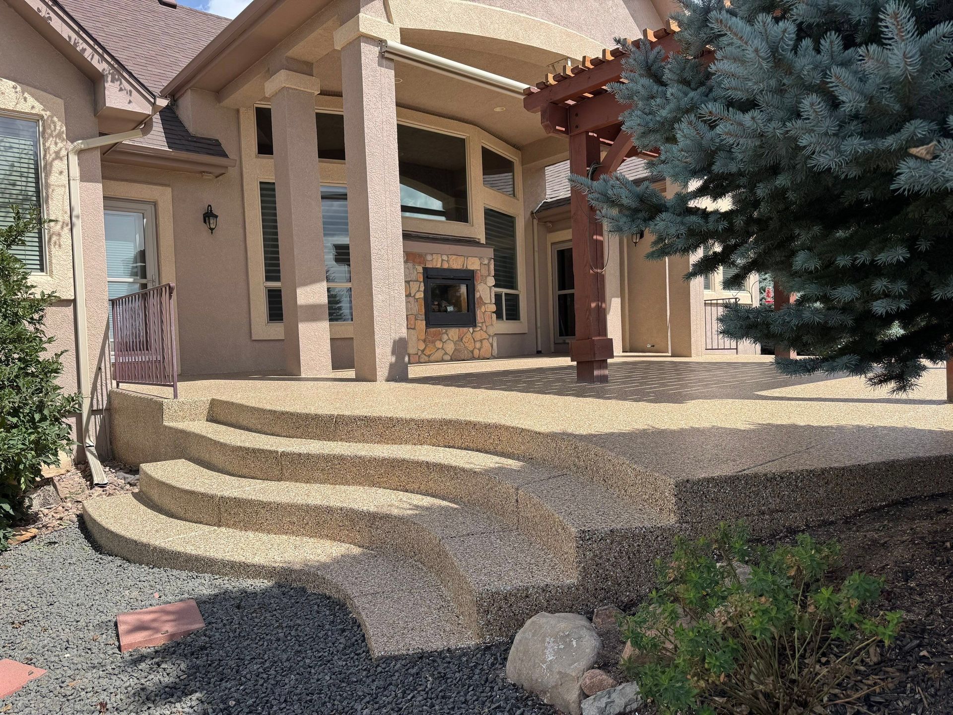 Stone front porch with curved steps, beige columns, and a large evergreen tree in the yard